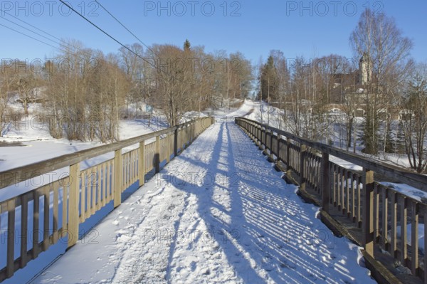 Old wooden walk bridge over river Koskenkylänjoki on a sunny winter day with snow covering the ground, Koskenkylä, Finland
