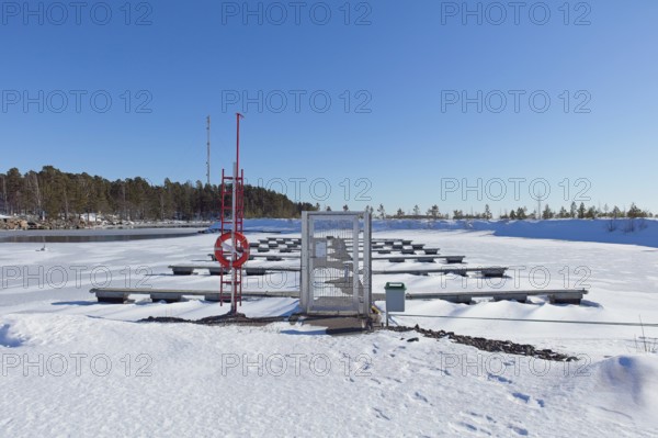 Empty marina with snow covered docks and ground with frozen sea ice on a cold winter day in sunny weather, Loviisa, Finland
