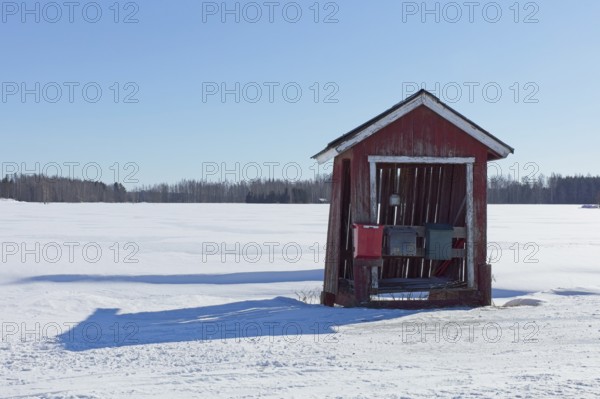 Old weathered red hut with three mail boxes by rural road in winter with snow covering the ground, Suurikylä, Finland