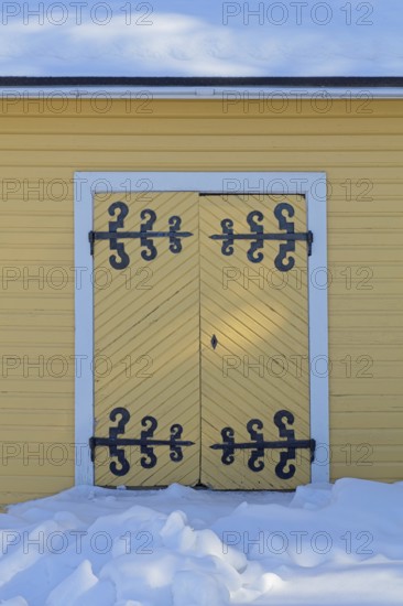 Old wooden double doors with wrought iron decorative hinges in winter with snow on the ground, Suurikylä, Finland
