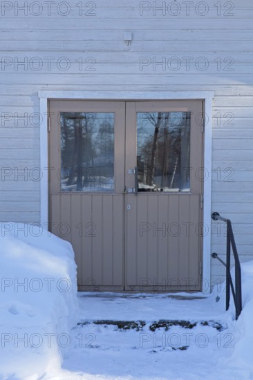 Double doors and steps on a old wood building in winter with snow on the ground, Vastila, Finland
