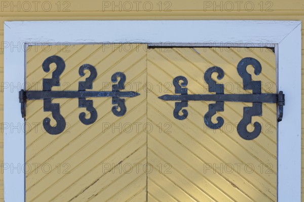 Closeup of old wrought iron decorative hinges on yellow painted wooden doors, Suurikylä, Finland