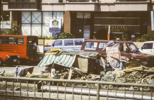 Homeless people have built an emergency shelter consisting of a wooden box and awning on the middle strip of a multi-lane road, behind it luxury apartments, Manila in 1995, Philippines