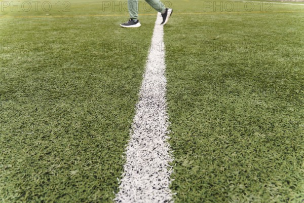 Person walking across a white line on a green artificial turf soccer field, representing progress or boundaries