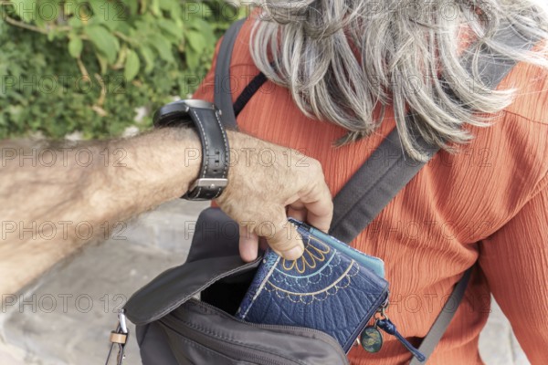 Ronda, malaga, spain Hand of a pickpocket discreetly removing a wallet from a person's backpack, representing theft and street crime