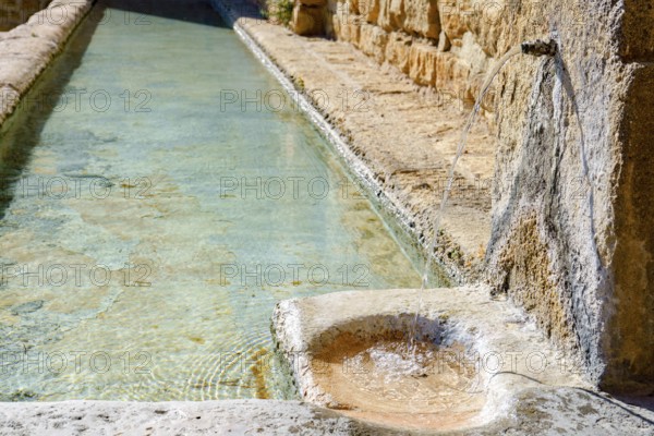 Ronda, malaga, spain Fresh, clear water flowing from an old stone spout into a historic rustic trough, creating gentle ripples in ronda, malaga, spain