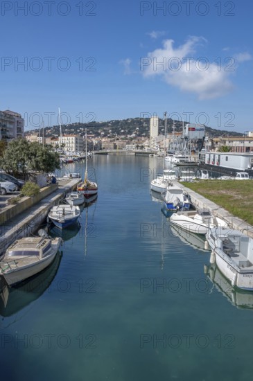 View from Pont des Dockers across the Canal de la Peyrade with moored boats along the quays towards the skyline of the city center with the wooded Mont Saint Clair in the background under a blue sky in Sete, Herault department, Occitanie region, France