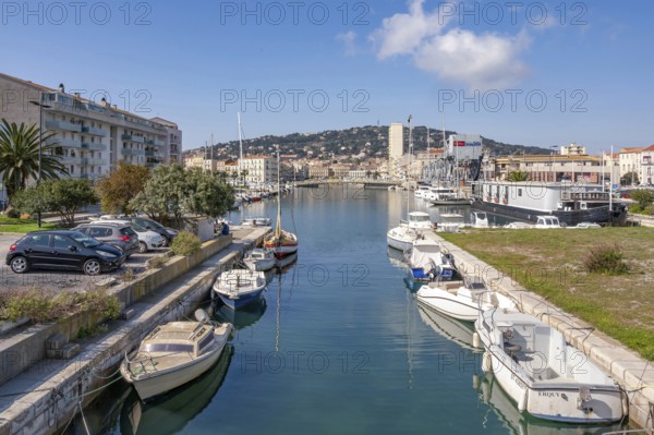 View from Pont des Dockers across the Canal de la Peyrade with moored boats along the quays towards the skyline of the city center with the wooded Mont Saint Clair in the background under a blue sky in Sete, Herault department, Occitanie region, France