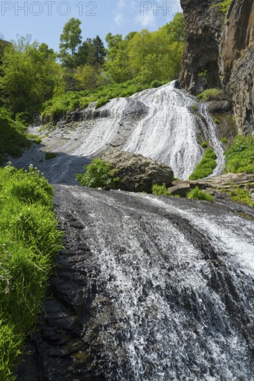 A multi-tiered waterfall and green plants create an idyllic natural landscape in the sun, Jermuk Waterfall, Vayots Dzor Province, Armenia