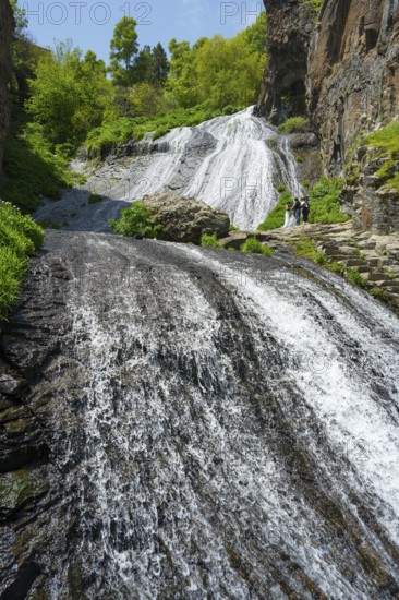 An extensive waterfall flows over rocks nestled in a green, sunny landscape, people at Jermuk Waterfall, Vayots Dzor Province, Vayots Dzor, Armenia