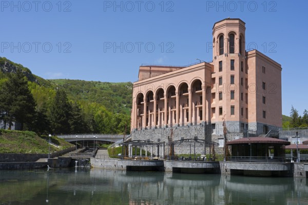 Large pink building with pillars on a river with a bridge surrounded by green hills and clear sky, Hotel Grand Resort Jermuk, Jermuk, health resort, Vayots Dzor province, Armenia