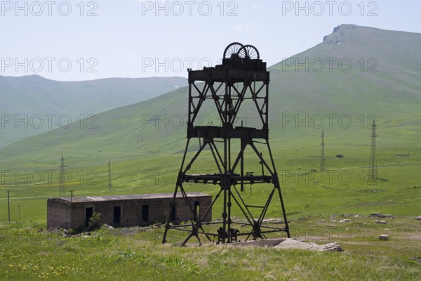 An abandoned structure in a green mountain landscape with ruined buildings and power poles, disused industrial plant, mining tower, located near the Vorotan Pass, Vorotan, Syunik Province, Syunik, Armenia