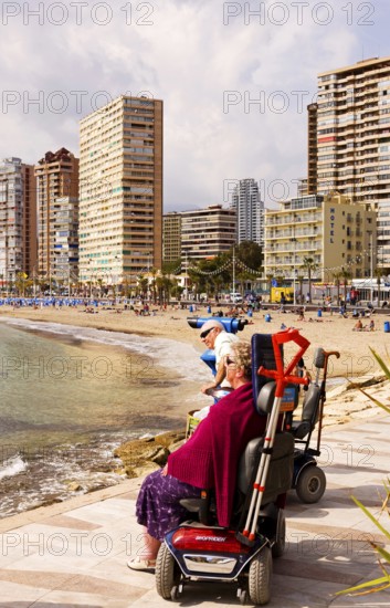 Two people in motorized wheelchairs, promenade on the beach, view of the high-rise skyline, Little Manhattan, skyscrapers, Benidorm, Valencia (region), Costa Blanca, Spain