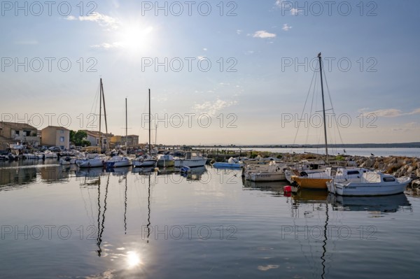 Atmospheric sun reflection on the quiet water surface of the harbor basin in La Pointe Courte, seen from the terrace of the Nene restaurant, with fishing boats, sailboats and the neighborhood houses in the background with a view of the Etang de Thau in Sete, Herault department, Occitanie region, France