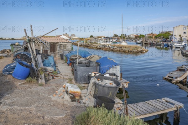 The traditional fishing port of La Pointe Courte with a small wooden shed, fishing nets, baskets and fishing gear on a narrow pier with wooden walkways and boats in the background under a clear blue sky in Sete, Herault department, Occitanie region, France
