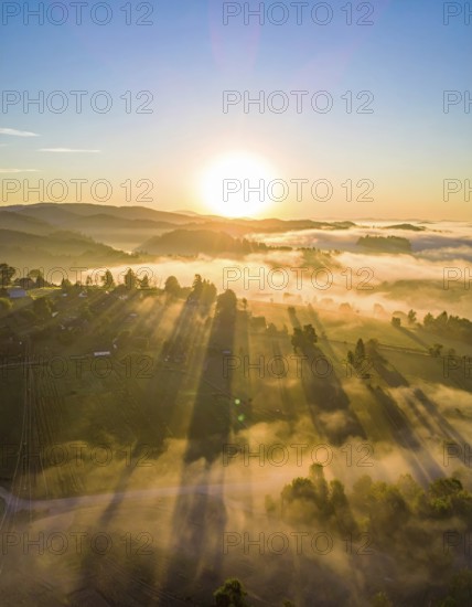 Sunrise over a fog covered village in a rural landscape, golden morning light, serene autumn atmosphere, hills and mountains in the background, AI generated