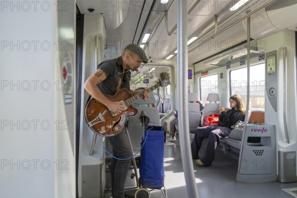 Musician busker playing guitar onboard train of Rodalia de Barcelona suburban rail network, Barcelona, Catalonia, Spain