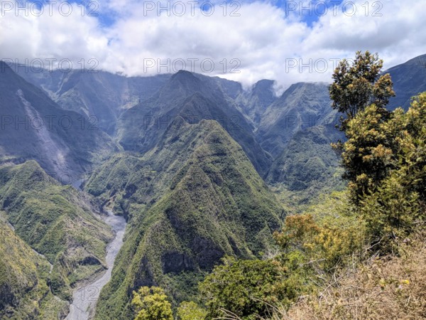 Breathtaking view of mountainous landscape with a river cutting through under a partly cloudy sky, La Réunion, France