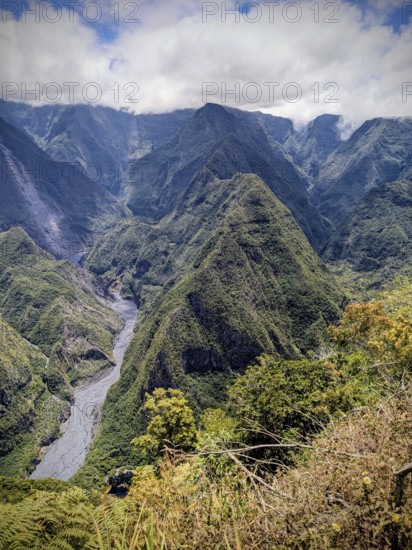 Expansive mountain range with deep valleys and lush greenery under thick clouds, La Réunion, France