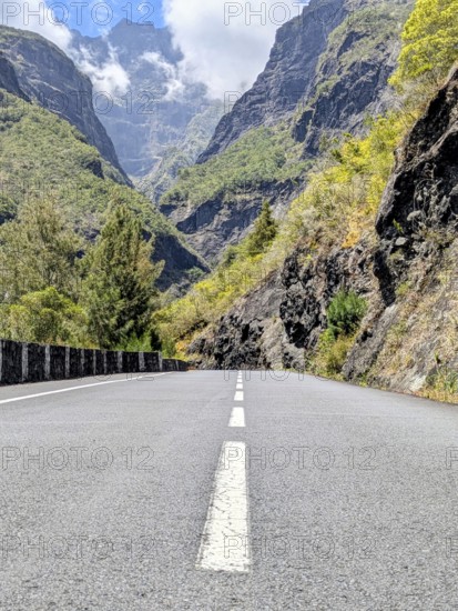 Paved road leading through a mountainous landscape beneath a cloudy sky, La Réunion, France