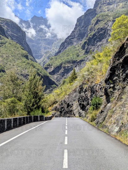 Winding road through mountains with towering peaks and a partly cloudy sky, La Réunion, France