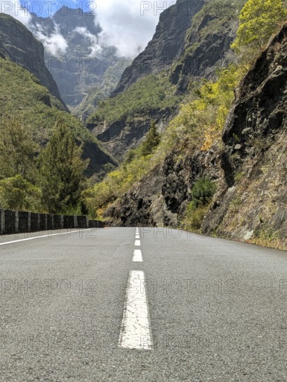 Mountain road leading towards tall peaks under a cloudy sky, La Réunion, France