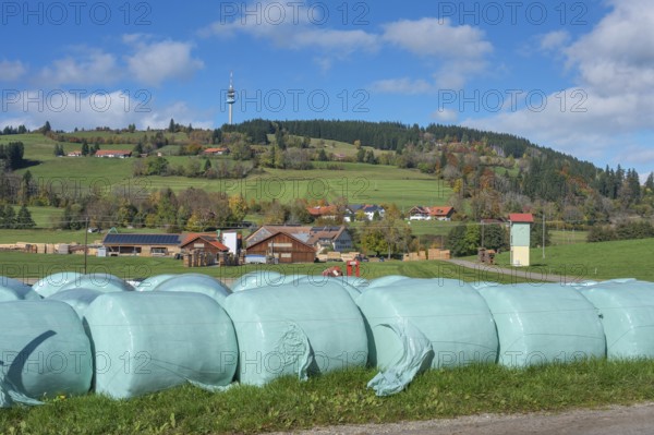 Blue sky with clouds, silage bales in front of the village of Masers under the mountain Blender with telecommunications tower near Kempten, Swabia, Bavaria, Germany