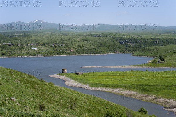 Winding river flows into a lake surrounded by green hills under a blue sky, Kechut Reservoir, Kushchi, Kush-Bilyak, Wajoz Dzor Province, Vayots Dzor, Armenia