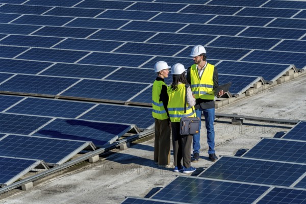 Group of diverse engineers in hard hats and vests working on a solar power station, discussing sustainability and renewable energy solutions for a greener future