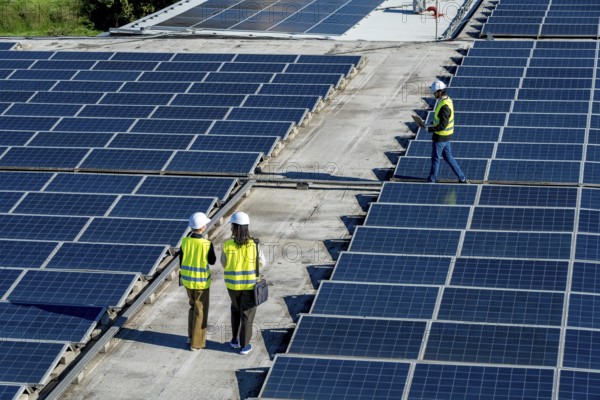 Engineers in hard hats and safety vests inspect rooftop solar panels, walking rows of pv modules during a sunny day to assess maintenance and performance of a renewable system