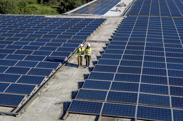 Engineers in hard hats and vests performing an inspection of a rooftop solar power plant, ensuring the efficiency and sustainability of renewable energy production
