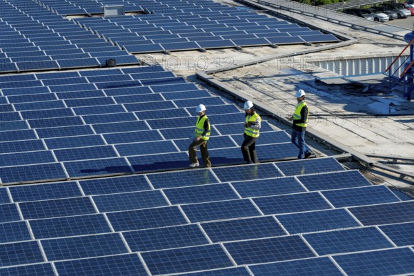 Engineers and maintenance workers are walking across an expansive array of solar panels installed on a commercial building roof, performing an inspection of the renewable energy system