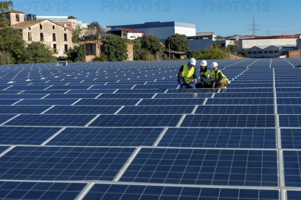 Engineers in hard hats and vests working on a vast solar panel field, reviewing data on a tablet, symbolizing sustainable energy development and clean power generation