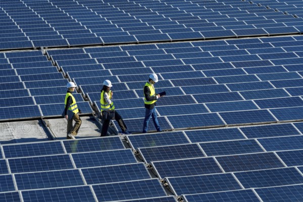 Engineers wearing safety helmets and vests are walking across a vast field of photovoltaic solar panels, examining the renewable energy installation and ensuring its optimal performance