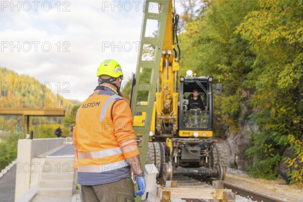 Construction worker with helmet looking at excavator working on rails, autumn environment, signal construction on the Hermann Hessebahn, Calw, Germany