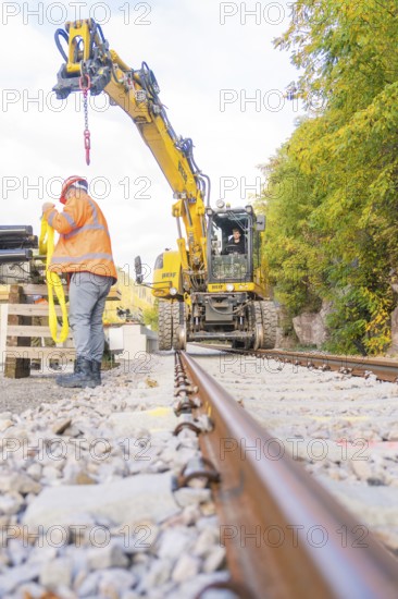 Excavator working on track, construction worker checking equipment, focus on rails, autumn landscape, signal construction at Hermann Hessebahn, Calw, Germany