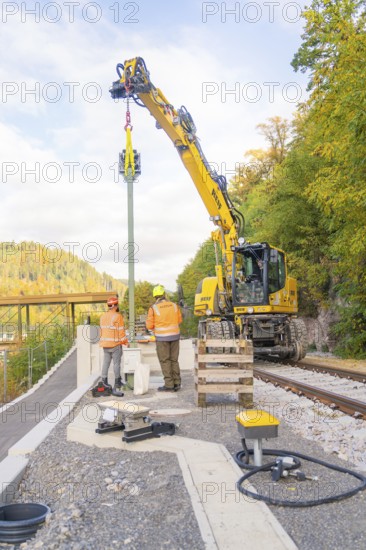 Excavator lifts object on railroad tracks, workers in protective clothing, signal construction at Hermann Hessebahn, Calw, Germany