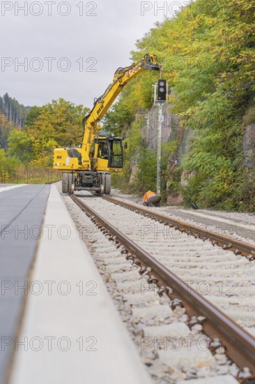 Yellow excavator on railroad tracks, surrounded by autumn trees, signal building on the Hermann Hessebahn, Calw, Germany