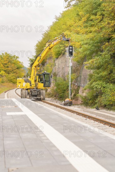 Yellow construction machine works on railroad tracks in a wooded area, Signalbau an der Hermann Hessebahn, Calw, Germany