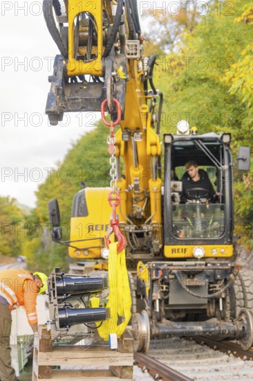 Close-up of an excavator with a worker, autumnal environment on railway tracks, signal construction on the Hermann Hessebahn, Calw, Germany