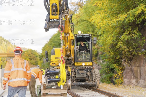 Excavator lifts objects on train tracks, construction workers talking, autumn environment, signal construction at Hermann Hessebahn, Calw, Germany