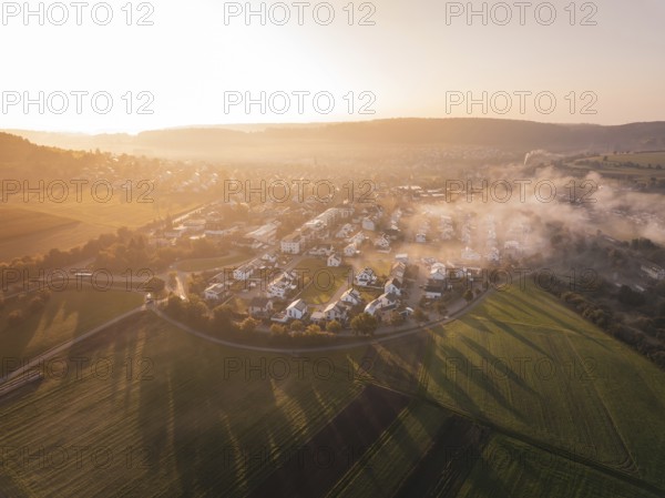 A village surrounded by fields in fog at sunrise with warm orange light, Calw Stammheim, Black Forest, Germany