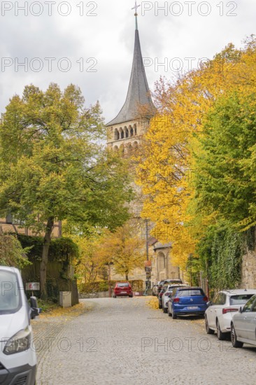 Church tower towers over an autumnal paved road with cars, Sindelfingen, Böblingen district, Germany