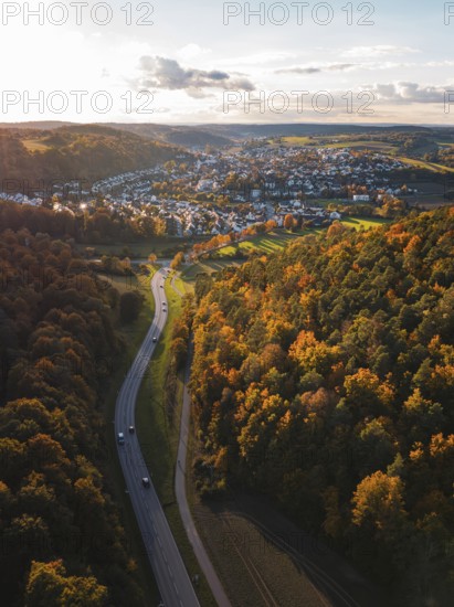A road snakes through autumn trees towards a small village, Aidlingen, Böblingen district, Germany