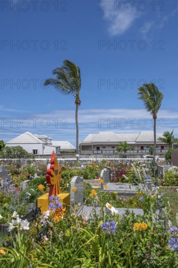 The flowery, multi-religious cemetery of Saint-Gilles-les-Hauts, with colorful graves and a Hindu shrine in the foreground, is dominated by tall palm trees, while in the background there are modern buildings under a blue sky, Saint-Gilles-les-Hauts, La Reunion, France