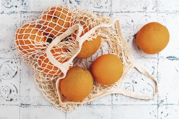 Oranges in a mesh bag, on a textured surface, sunlight, no people