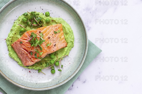 Delicious grilled salmon is placed elegantly on creamy green pea puree. Fresh microgreens and peas add a bright touch, creating an appetizing dish perfect for any meal