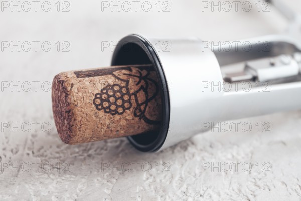A shiny silver corkscrew rests on a light textured surface, with a wine cork partially inserted, indicating its readiness for opening a bottle. The scene is simple and focused on the tool