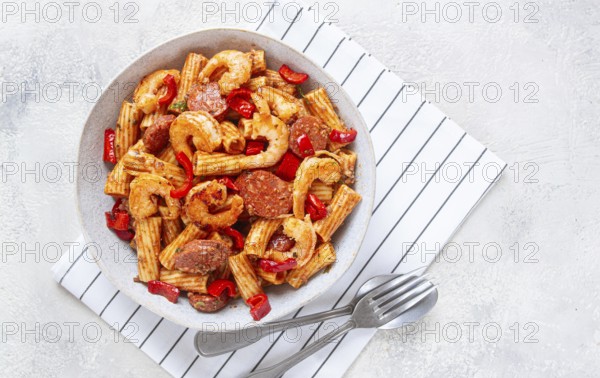 Jambalaya pasta with shrimp and sausages, cooked with bell pepper in a frying pan, homemade, on a marble kitchen countertop