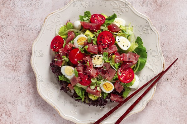 Salad with fresh tuna, cherry tomatoes and quail eggs and avacado, served with chopsticks